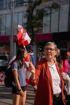 Una mujer que agita la bandera canadiense mientras camina por la calle.
