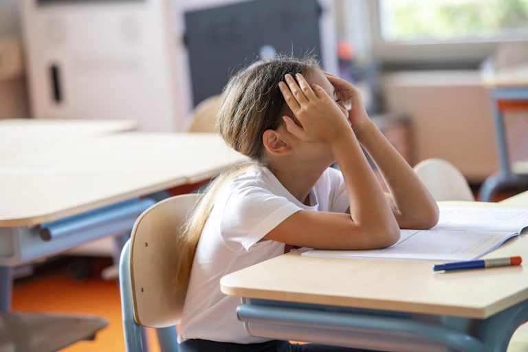 Girl at school desk holds her head in her hands.