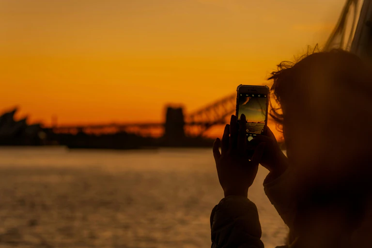 Someone photographs Sydney Harbour at sunset.
