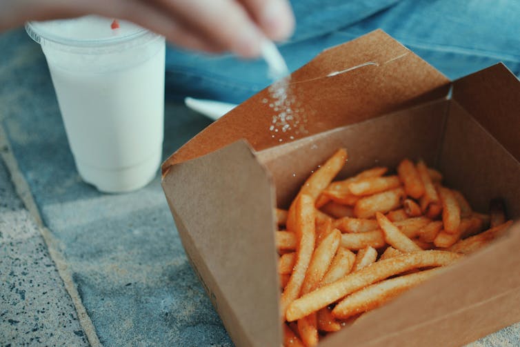 A box of takeaway chips being sprinkled with salt