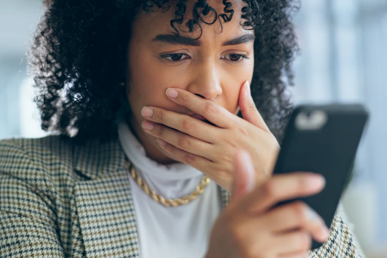 A woman with her hand over her mouth looks at her phone