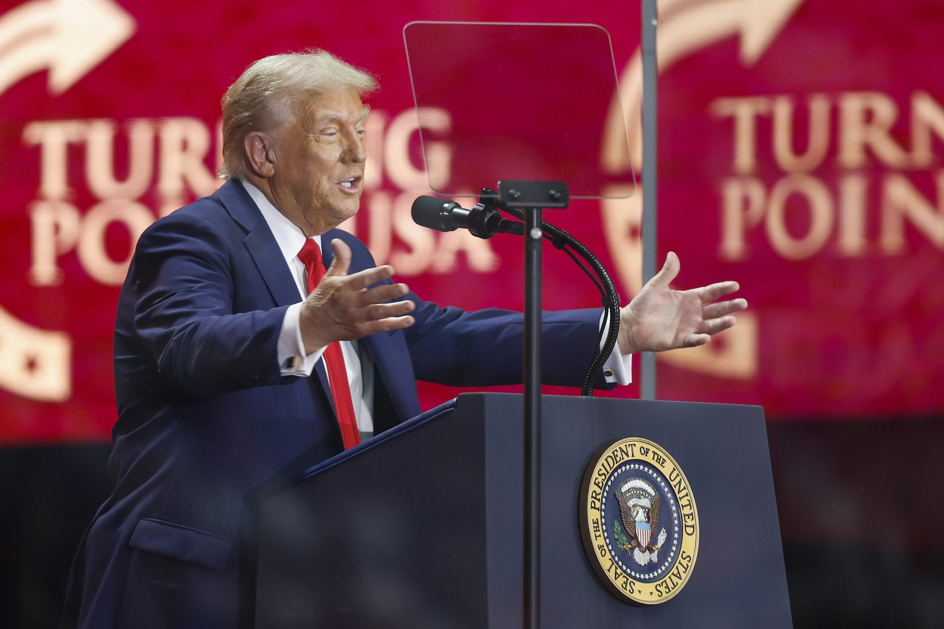 Donald Trump holds out his arms while speaking at a lectern at a Truning Point event September 21 2025.