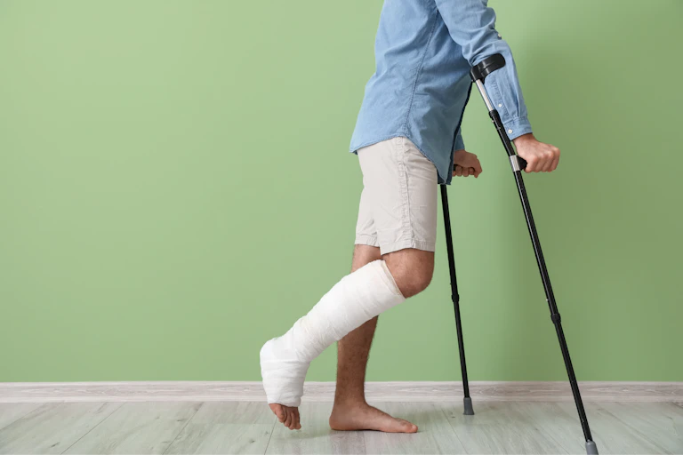 A man with a cast on his right leg uses a pair of crutches to walk.