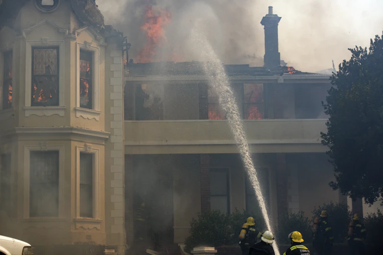 A jet of water aimed at a building, with flames and smoke visible