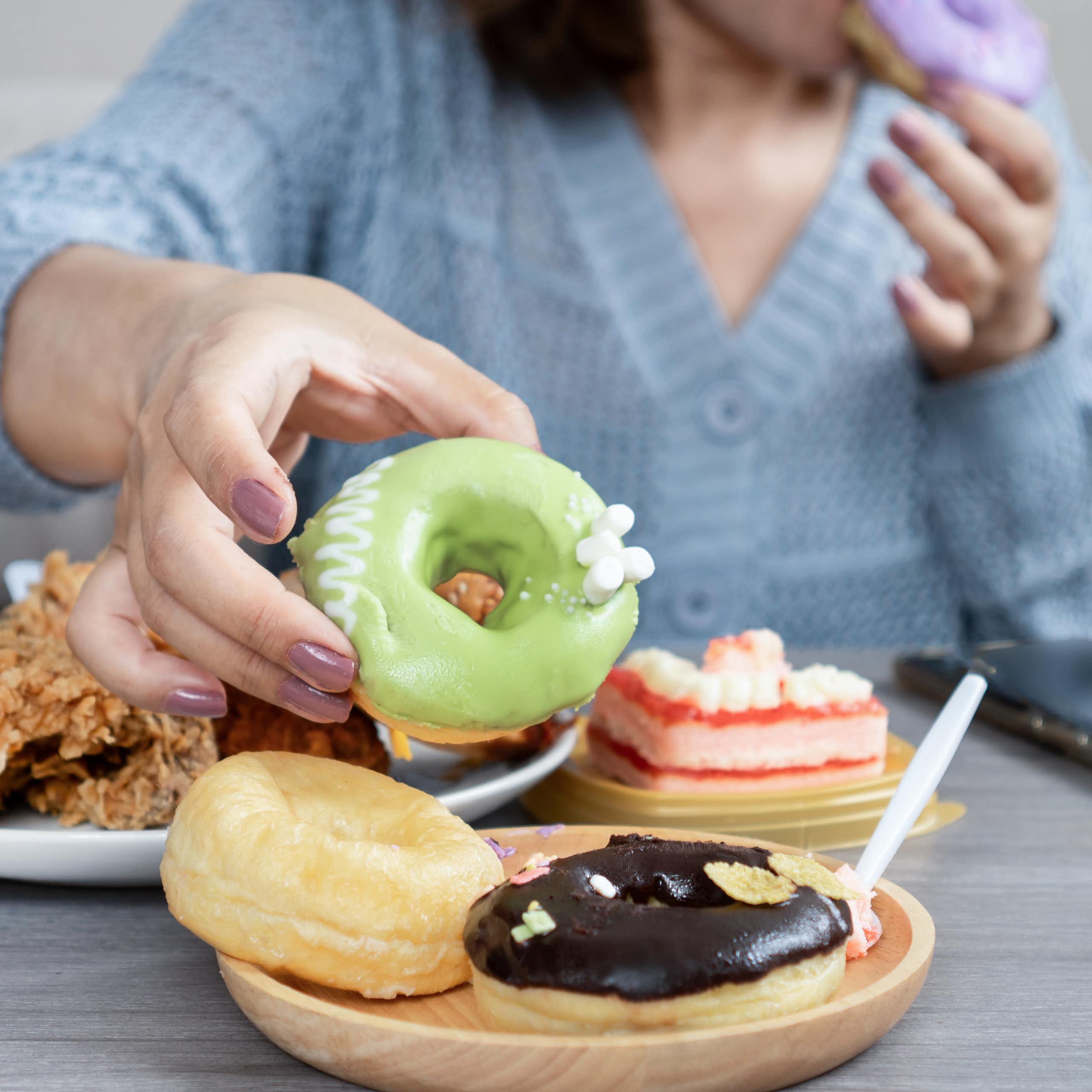 woman sitting at a table with colorful pastries and fried food.