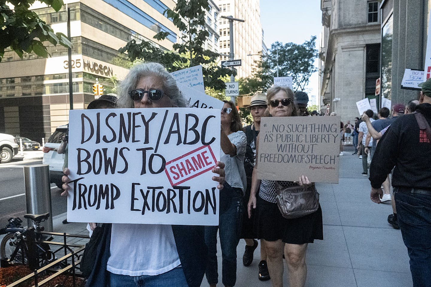 Elderly female holds sign reading 'Disney/ABC bows to Trump extortion.'
