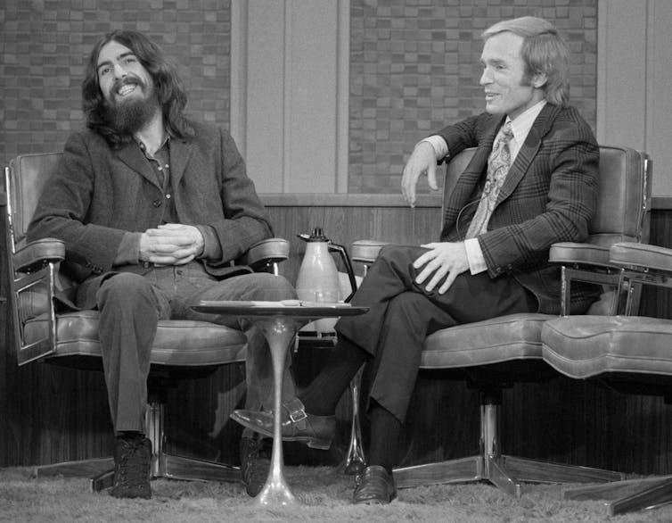 Imagen en blanco y negro de dos hombres sentados en sillas y charlando en la televisión.