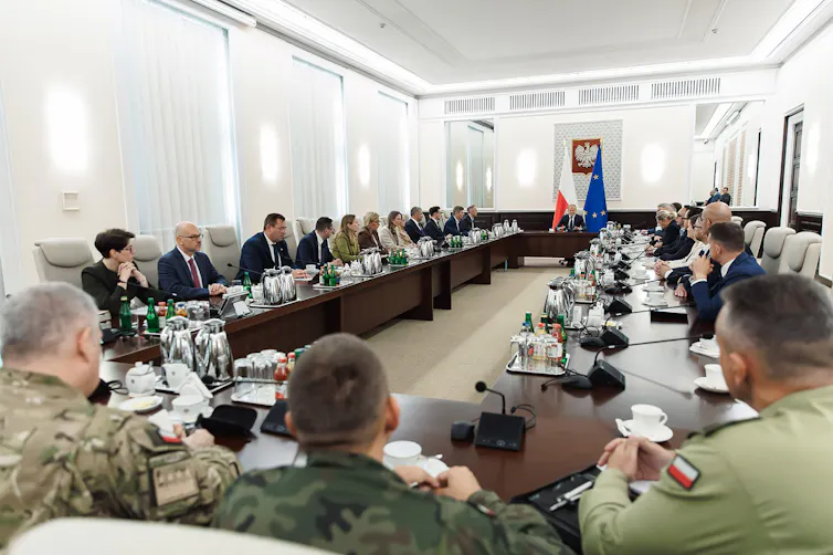 Poland's prime minister, Donald Tusk sits at the head of a long table with Polish politicians, civil servants and army personnel.