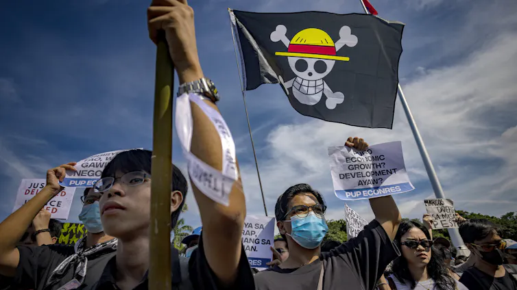Protesters, some in masks, hold aloft a flag with a skull in a straw hat.