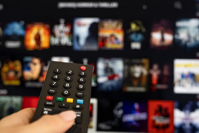 A woman's hand holding a remote with a screen in the background.