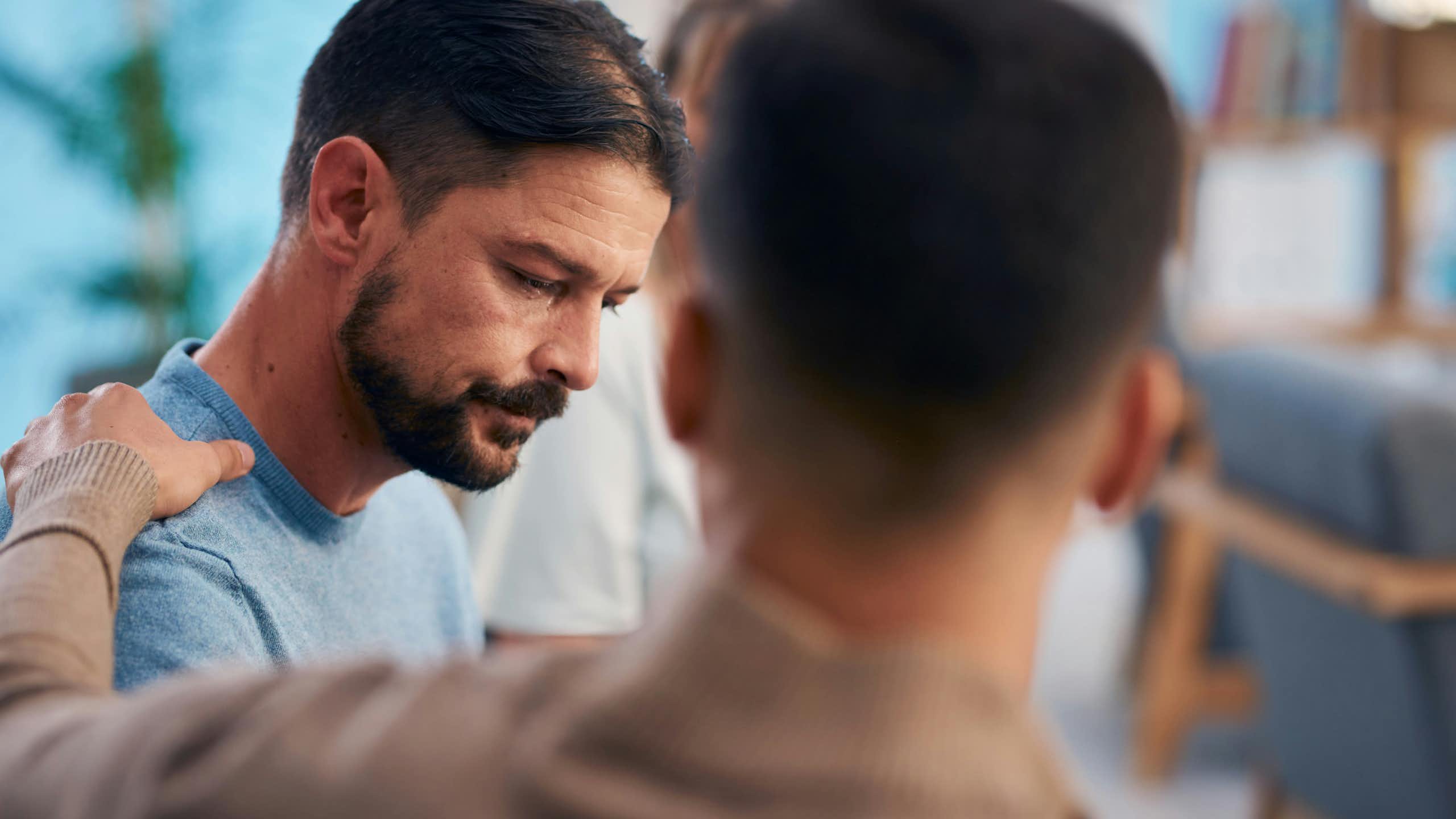A man rests his hand on another man's shoulder