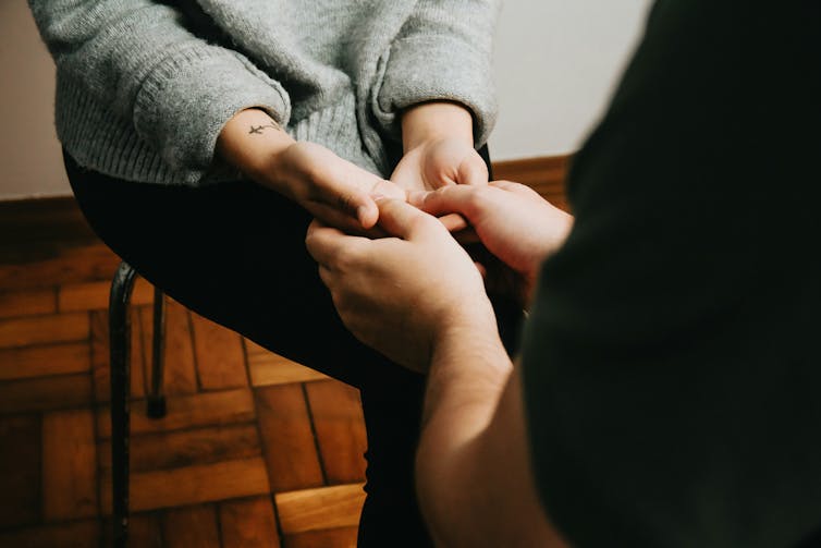 Un crup de una persona sosteniendo las manos de otra persona, sentada sobre ellas