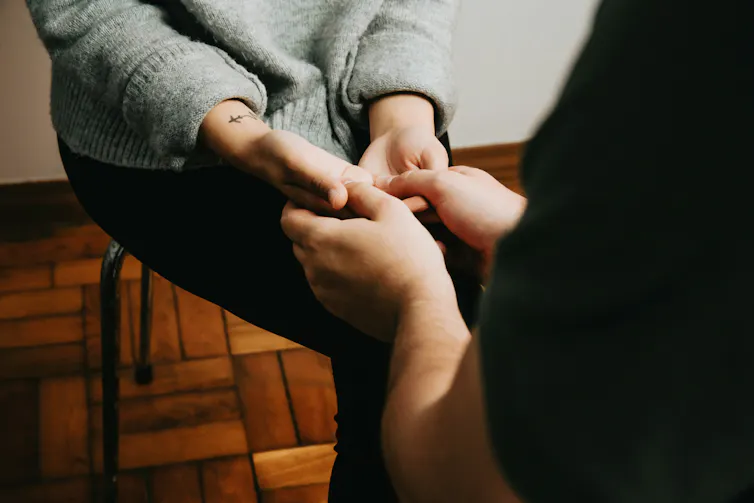 Closeup of one person holding another person's hands, who is sitting across from them