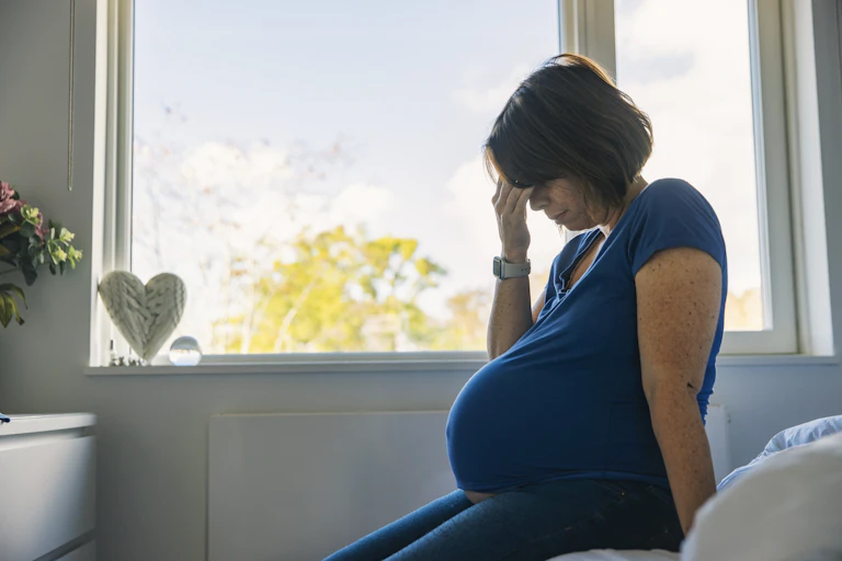 Pregnant woman sits on the side of the bed