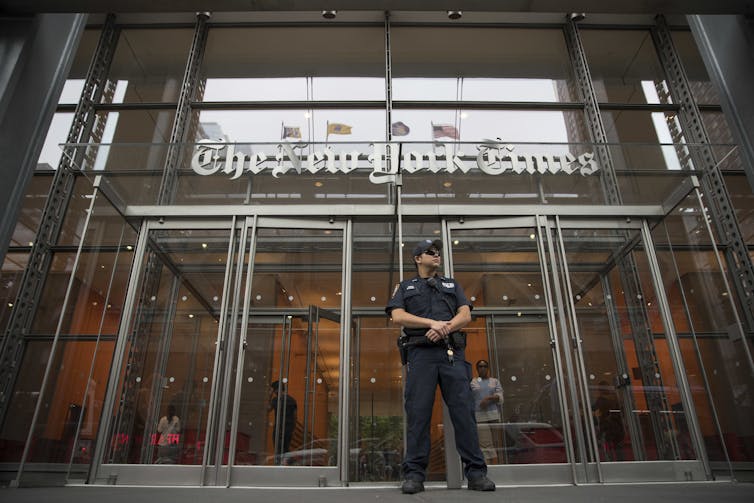 A police officer stands in front of the glass exterior of the New York Times building.