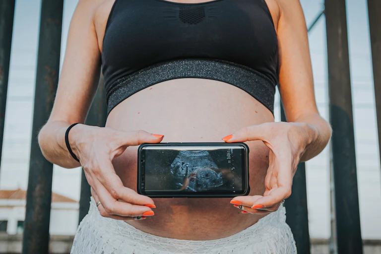 Échographie d'un bébé sur l'écran d'un téléphone portable tenu devant le ventre d'une femme enceinte.