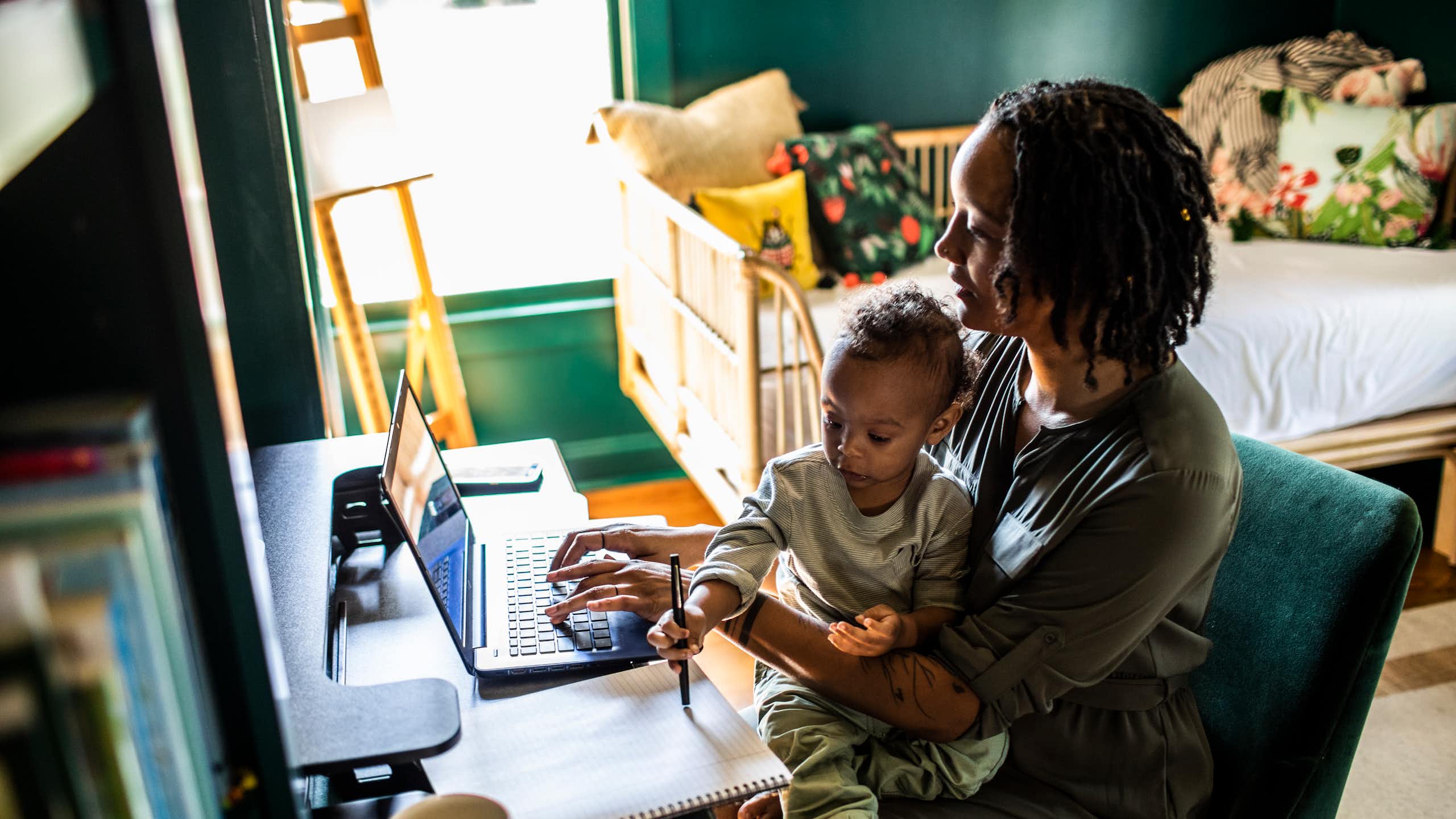 Une femme travaille à domicile tout en tenant un tout-petit dans ses bras.
