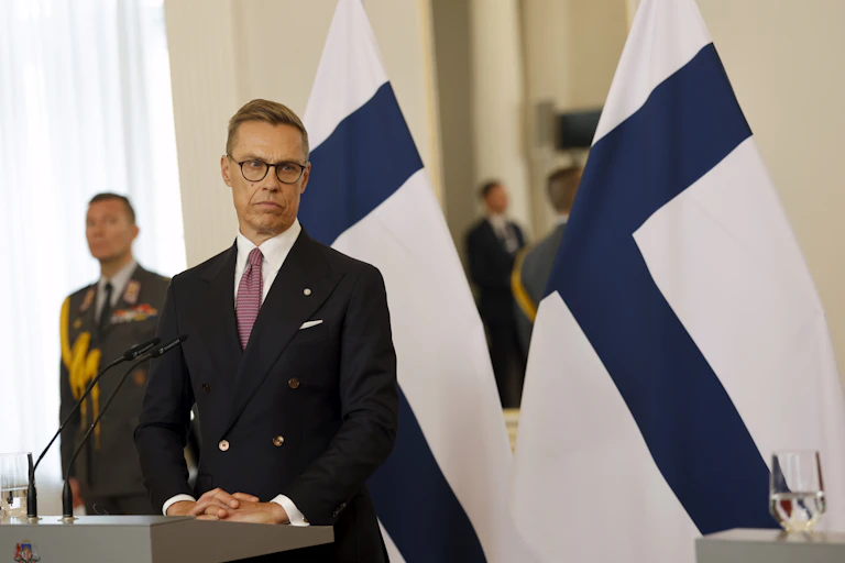 Alexander Stubb speaks at a press conference in front of Finland's national flag.