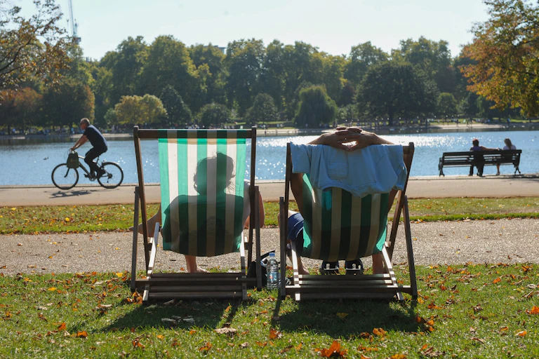two people relaxing in deckchairs in front of a river on a hot day in the uk
