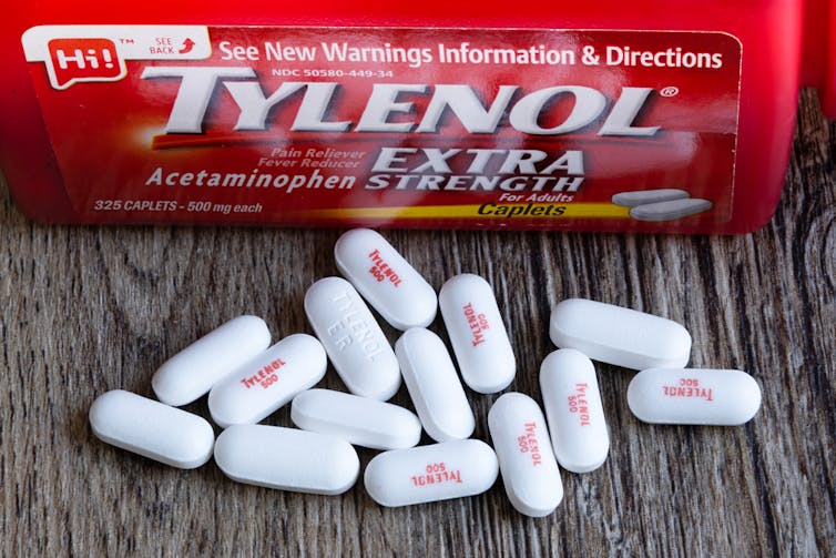 A Tylenol container with some Tylenol pills in the foreground.