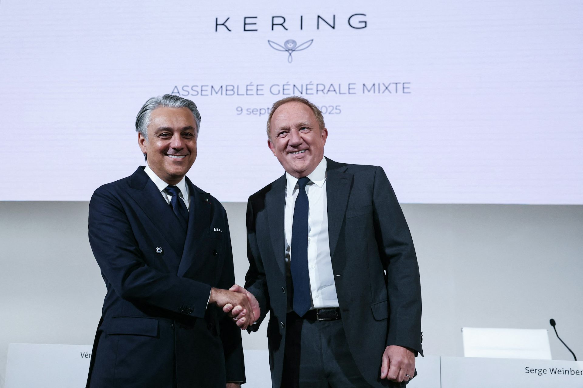 A handshake between Luca de Meo (left) and François-Henri Pinault (right) in front of a Kering logo.