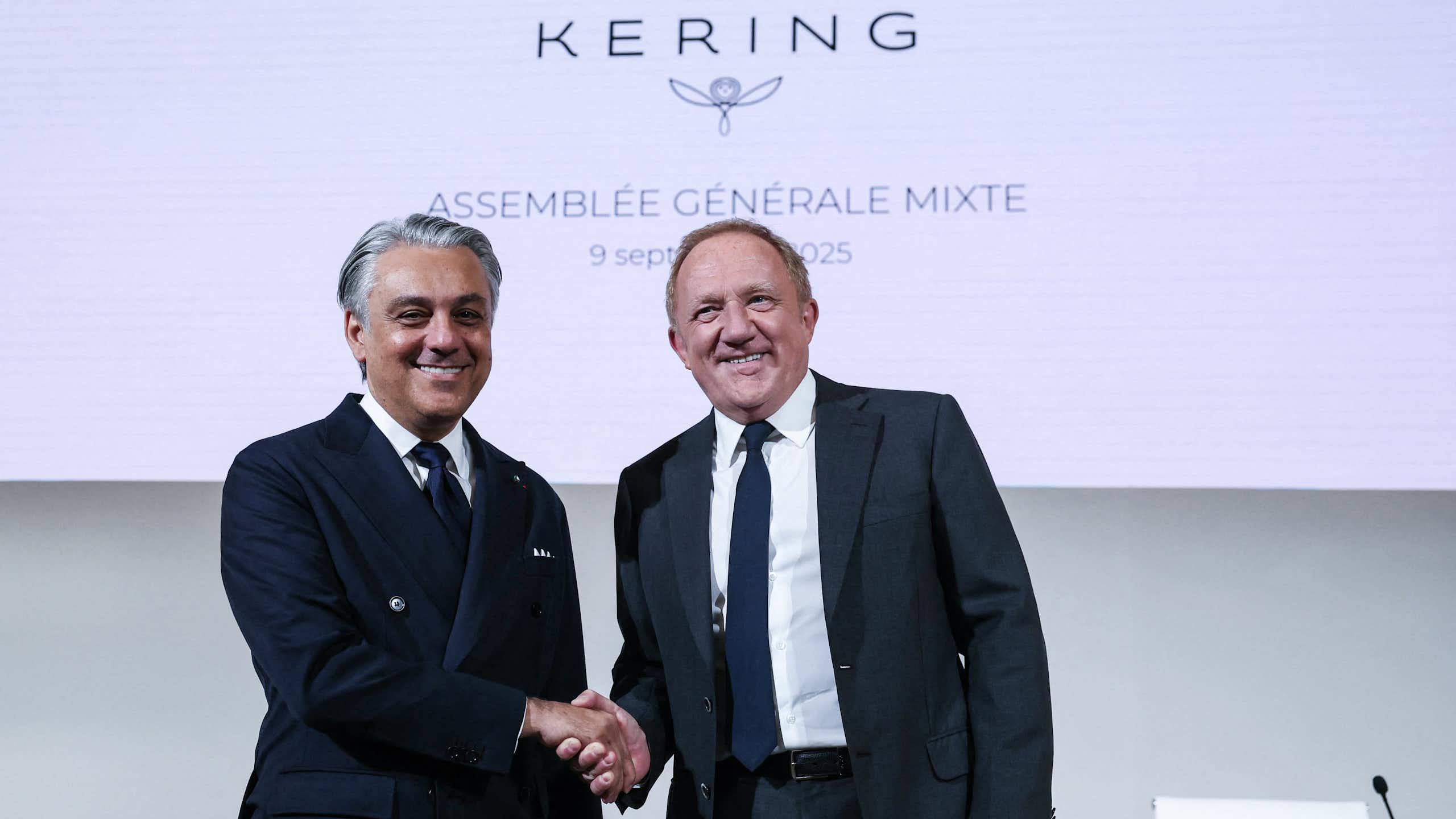 A handshake between Luca de Meo (left) and François-Henri Pinault (right) in front of a Kering logo.