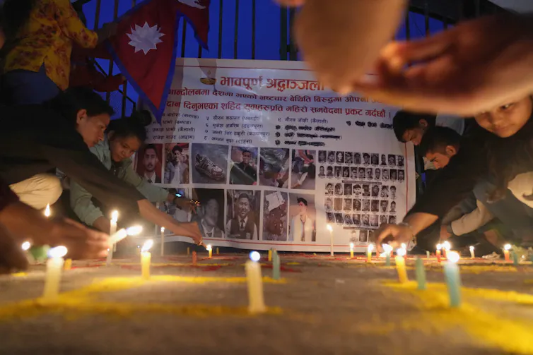 Candles are lit in front of a list of names and photographs.