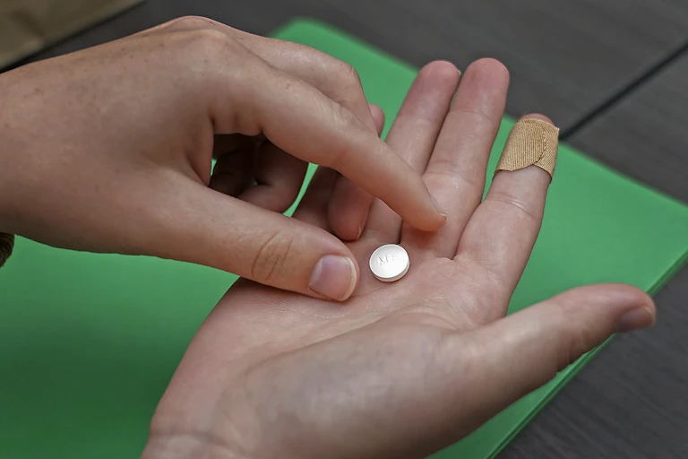 A person picks up one small white pill from the middle of their other hand.