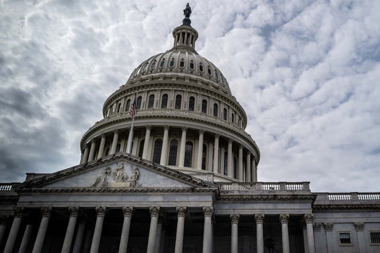 A large, white, domed building with clouds behind it.