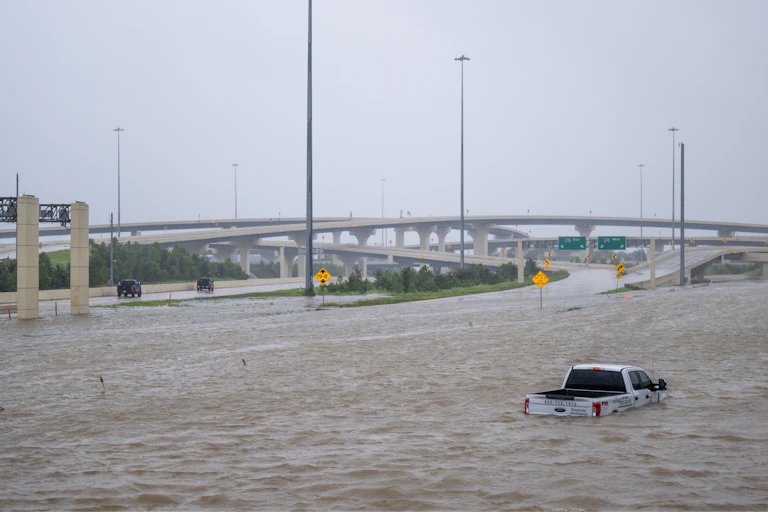 A truck is submerged above its tires in water on a highway.