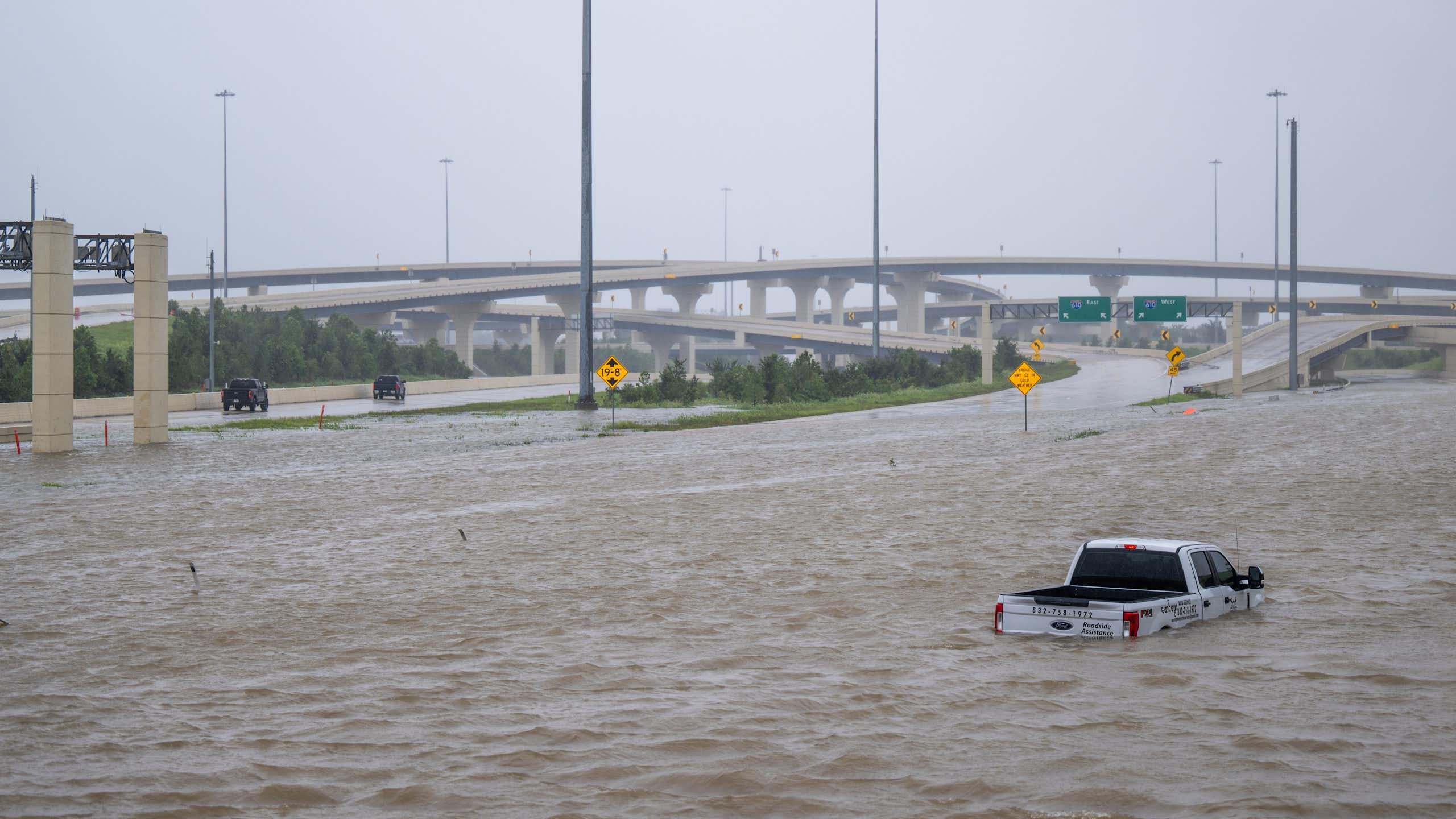 A truck is submerged above its tires in water on a highway.