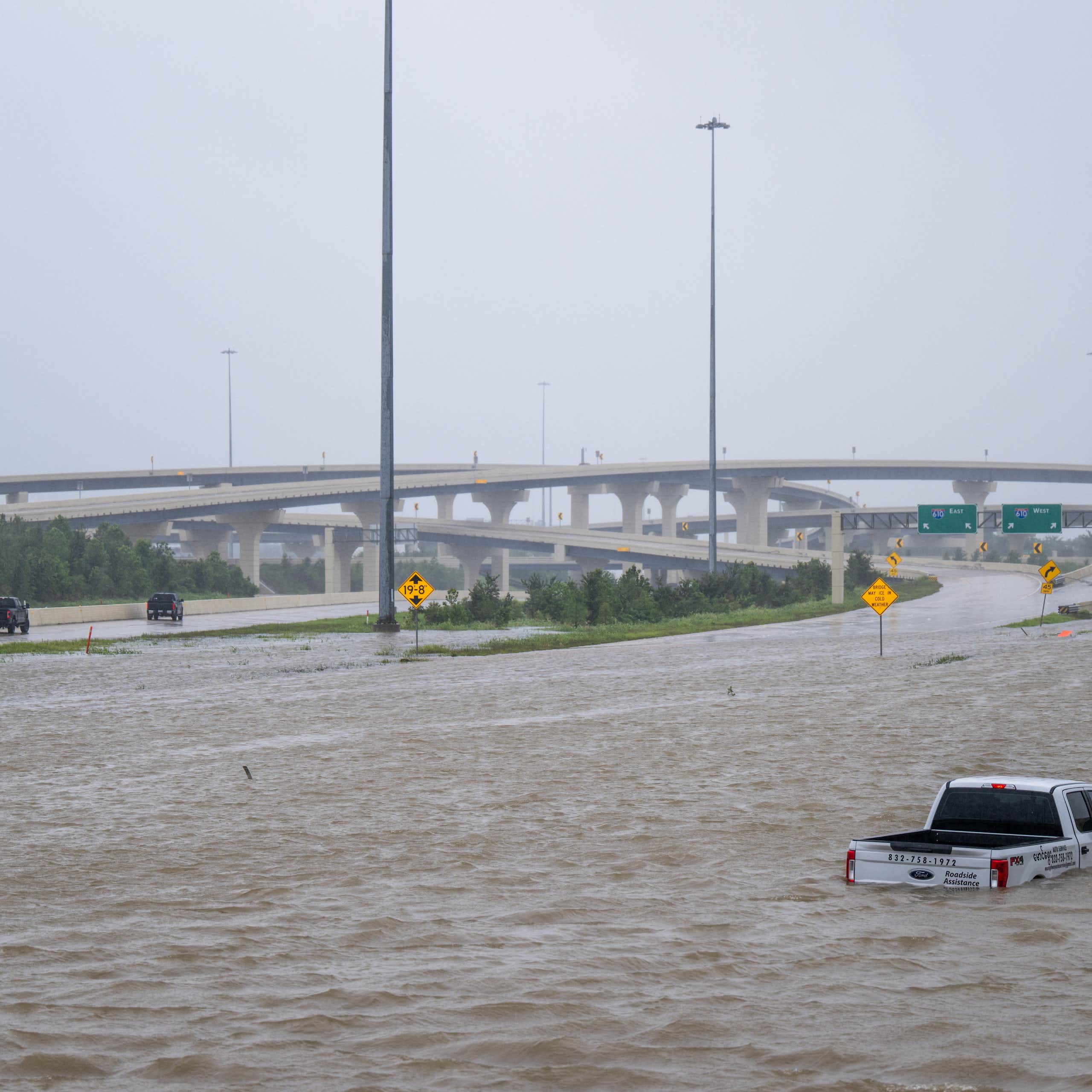 A truck is submerged above its tires in water on a highway.