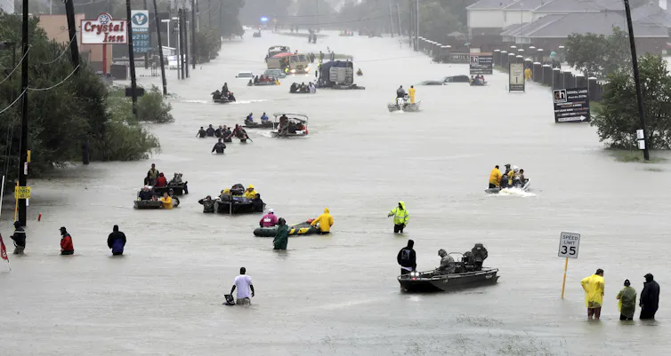 People and small boats move along a flooded street.