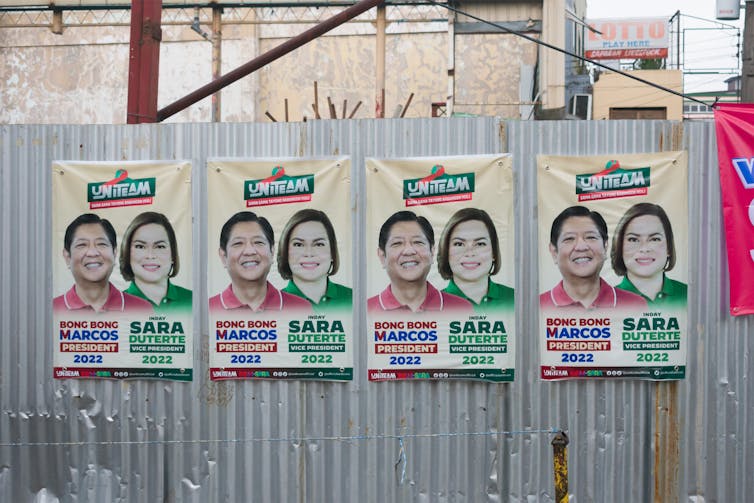 Campaign posters of candidates Ferdinand Marcos Jr and Sara Duterte taped to a corrugated iron sheet wall.
