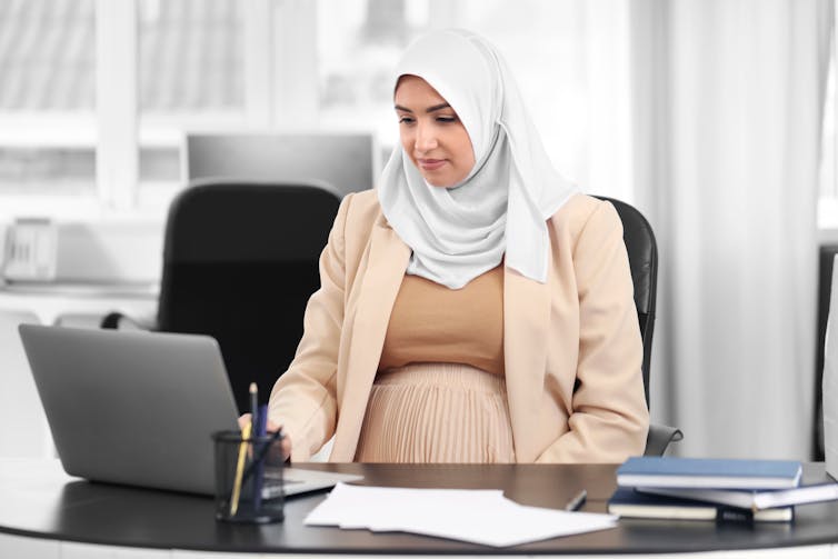 Pregnant woman in hijab at desk with laptop