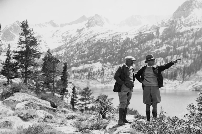 Une photo en noir et blanc de deux promeneurs dans la première moitié du XXe siècle en randonnée dans les montagnes.