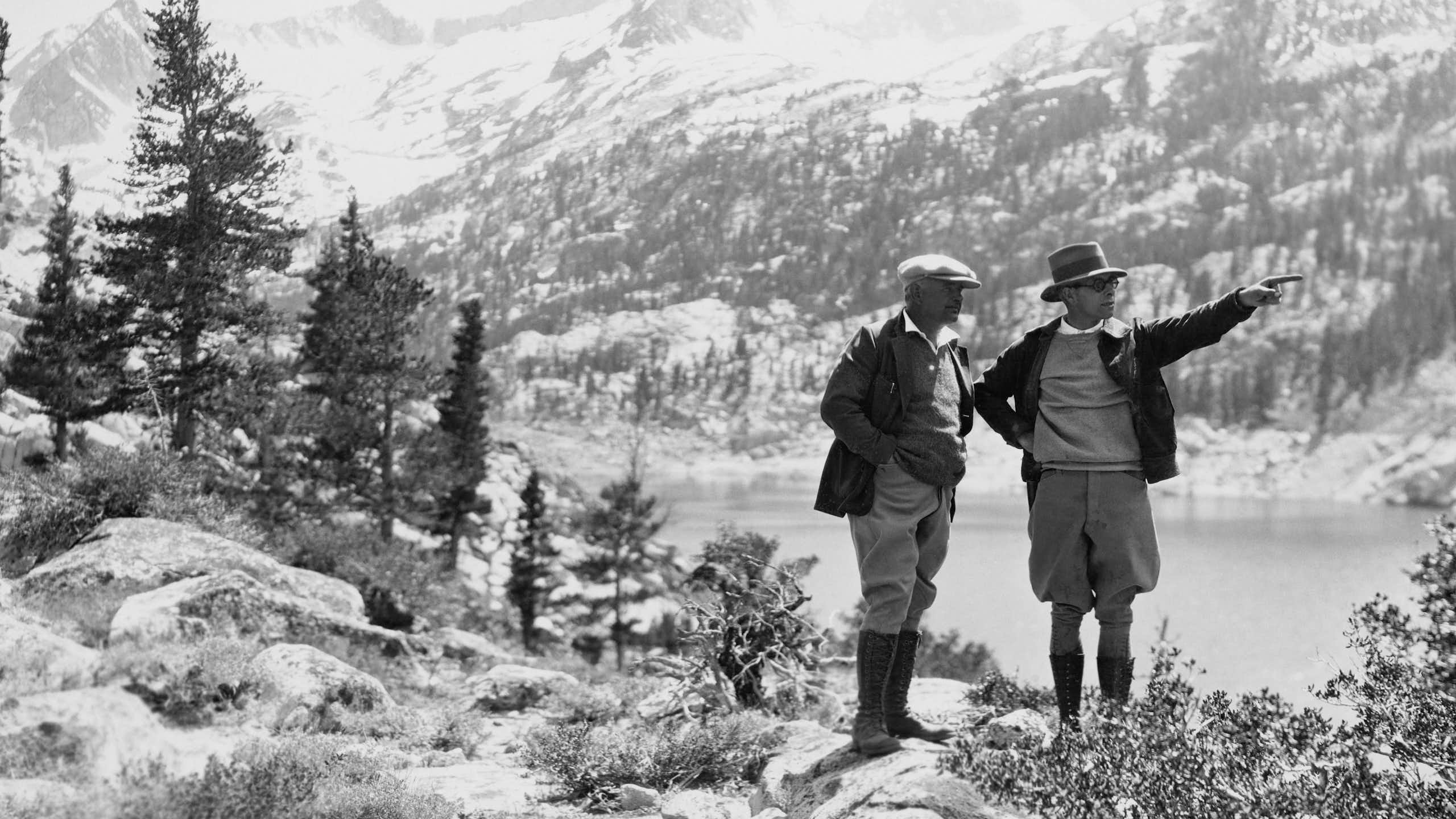 Une photo en noir et blanc de deux promeneurs dans la première moitié du XXe siècle en randonnée dans les montagnes.