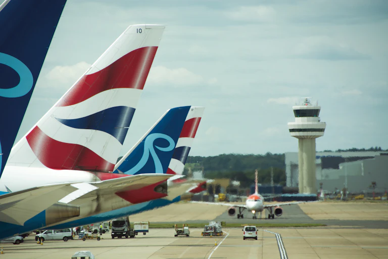 tails of planes parked on the apron at gatwick airport with the control tower in the background