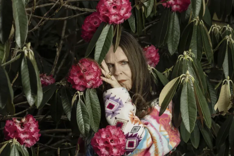 A woman in brightly coloured clothes standing in a rhododendron bush.