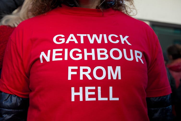 woman wearing a red t-shirt reading gatwick neighbour from hell.