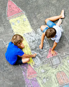 Two boys drawing a castle with crayons on the street.