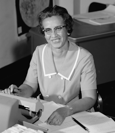 Photo noir et blanc de Katherine Johnson, elle est assise à son bureau devant une machine à écrire ou à calculer.