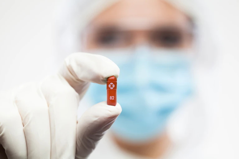 pharmacist wearing a mask and holding up a small red pill