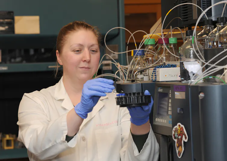 Person wearing white lab coat and nitrile gloves handling lab equipment.