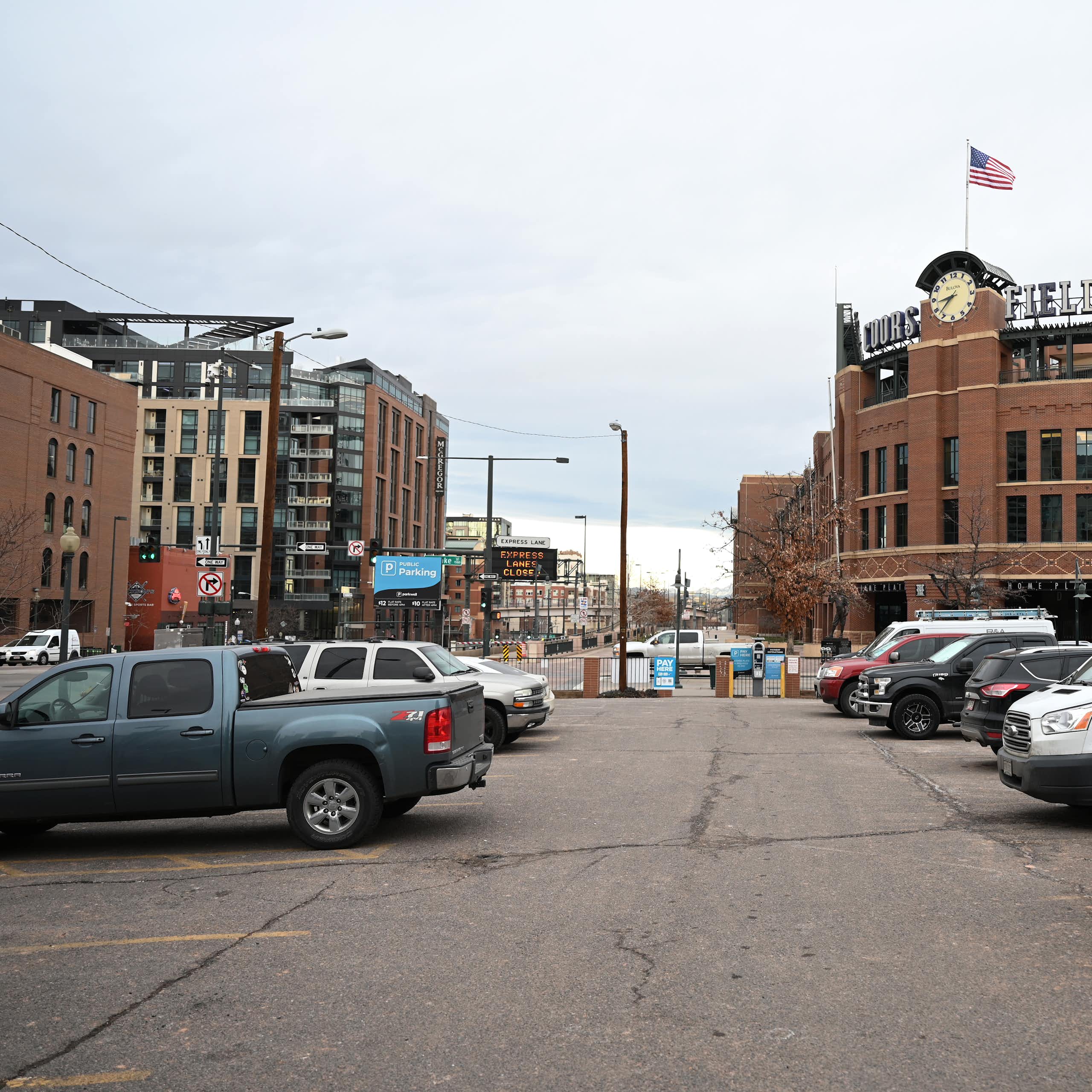 A parking lot near a stadium, Coors Field. Most of the spots are filled by cars of various shapes and sizes - especially trucks.