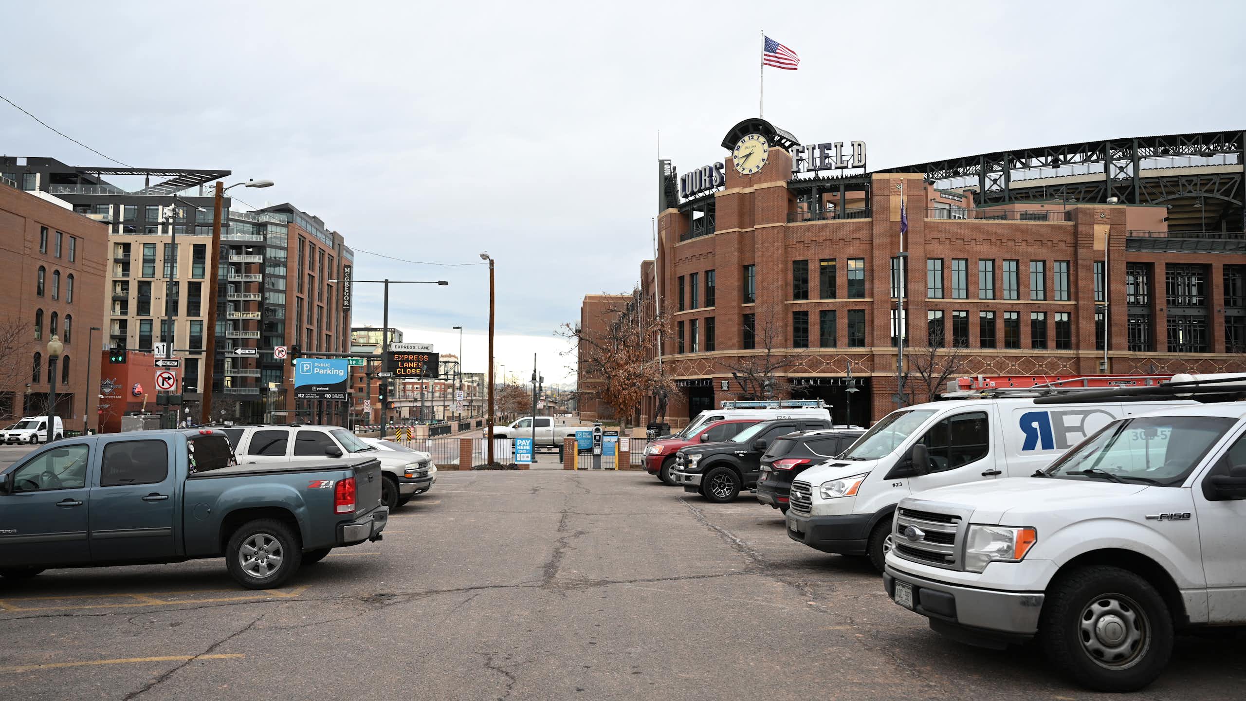 A parking lot near a stadium, Coors Field. Most of the spots are filled by cars of various shapes and sizes - especially trucks.