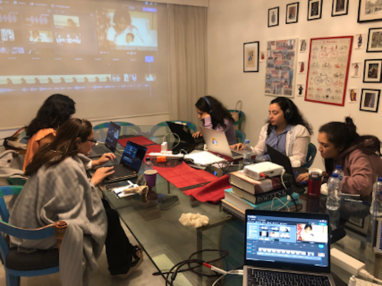 Six women surround a table where they work on multimedia projects.