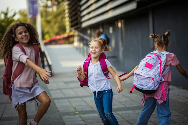 Three girls wearing school backpacks are walking happily on the street.