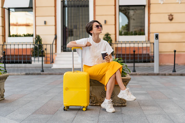 A woman wearing a bright yellow skirt that matches with her yellow suitcase sits and admires her surroundings.