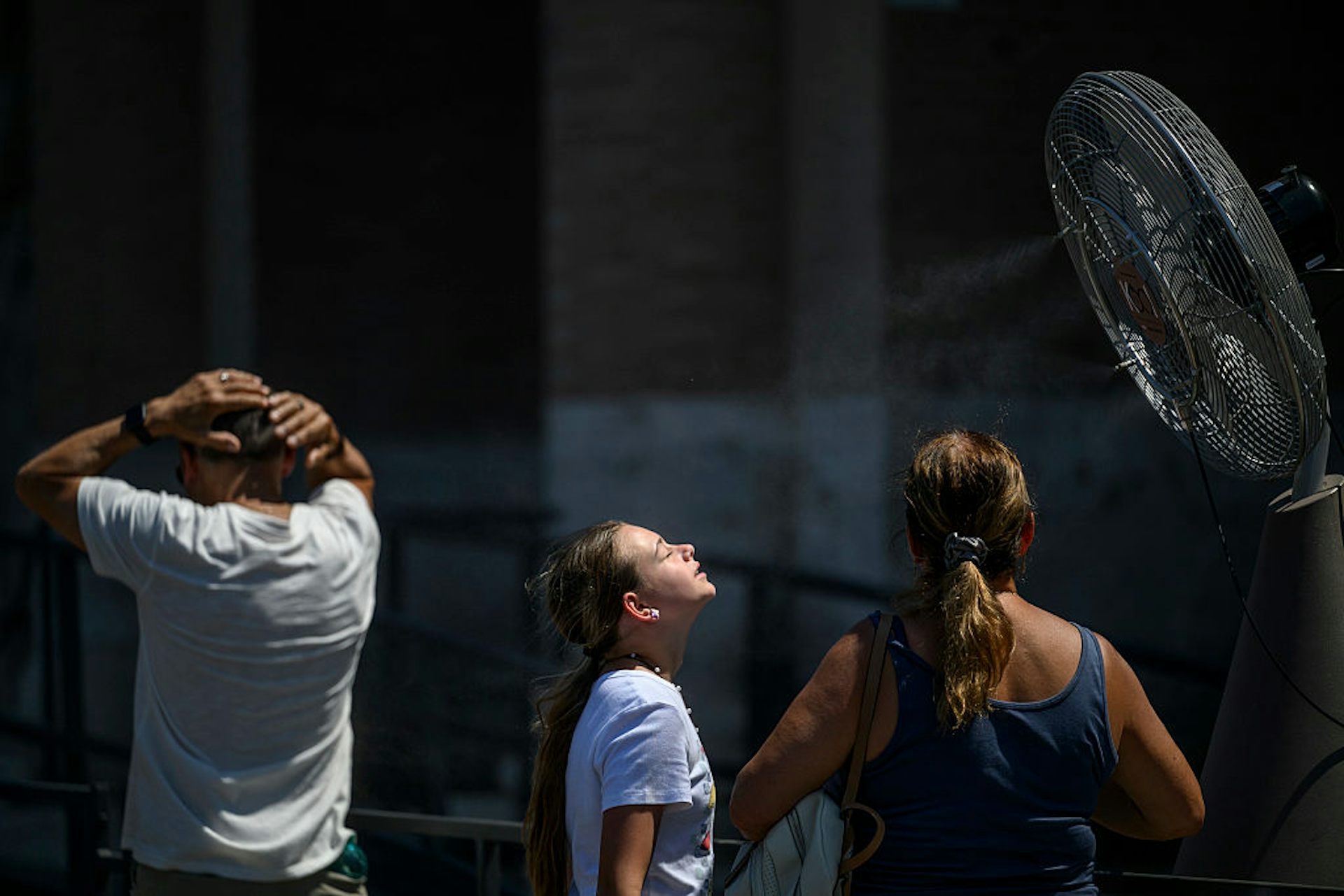 A girl and a woman stand in front of a giant fan.